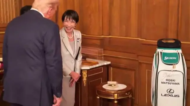 Takaichi smiling as she looks at Trump, who's backfacing the camera. Beside them is a green and white golf bag