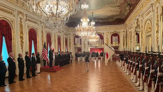 Trump and Takaichi stand in the middle of the room, in front of a line Japanese soldiers