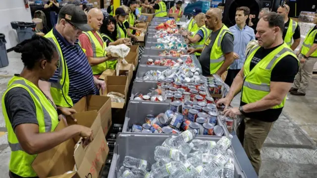 Workers in neon vests stand near bins of water and canned food