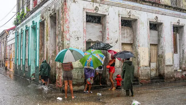 Residents standing around, waiting in the rain for food, on a street in Cuba