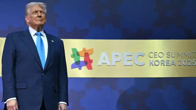 Donald Trump standing on stage with the logo of the Apec CEO Summit in the blue background