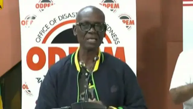 Demond Mckenzie wears glasses and a black jacket speaking at a microphone