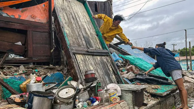 A woman in a yellow jacket holds out a hand to another person with kitchen supplies visible outside