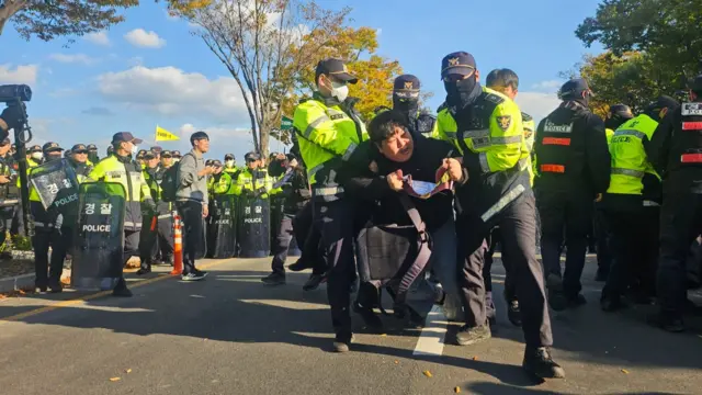 A man being lifted by police officers in neon yellow jackets