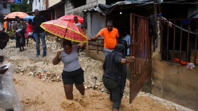 people with umbrellas wading through shin-high water in a flooded street
