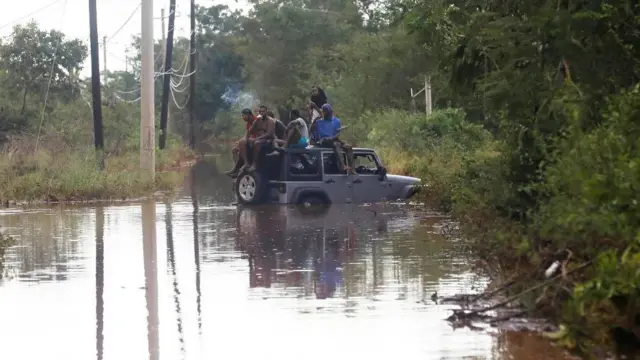 People sit on the roof of a vehicle riding on a flooded road