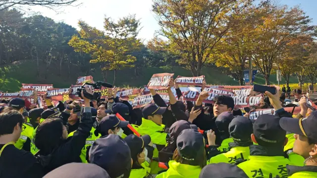 A sea of protesters holding up banners pushing up against police officers in neon jackets
