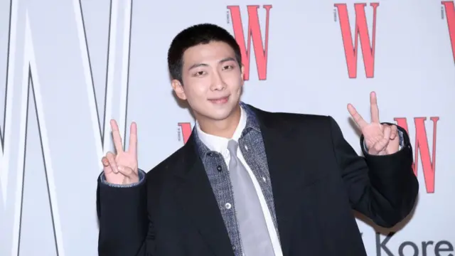 RM wearing a blazer flashing two peace signs
