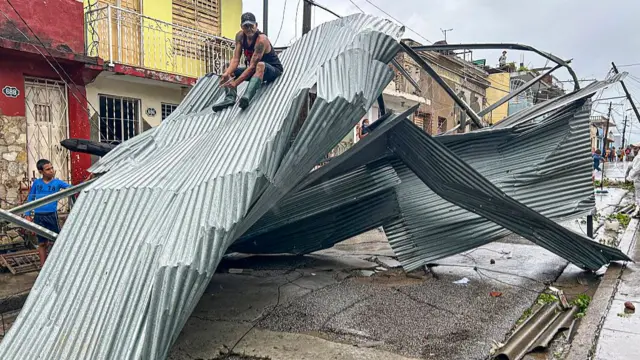 A man sits on a top of a very large piece of corrugated iron which is twisted
