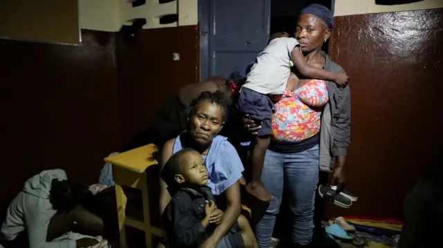 Children are held by adults in a classroom at nighttime.