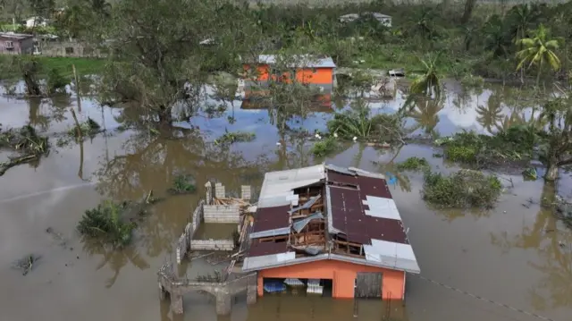 A house is at the centre of the image and has been almost fully submerged in flood water