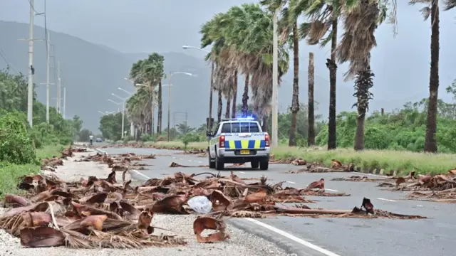 A police car drives down a road littered with debris