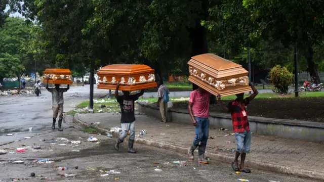 four people carrying three empty coffins through street filled with trash