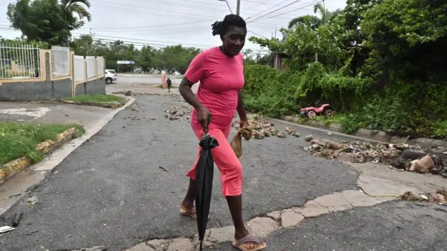 A woman wearing pink clothes walks among rocks and debris left behind by Hurricane Melissa in Kingston, Jamaica, 28 October 2025.