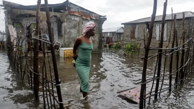 woman standing in shin-high water near a small concrete home