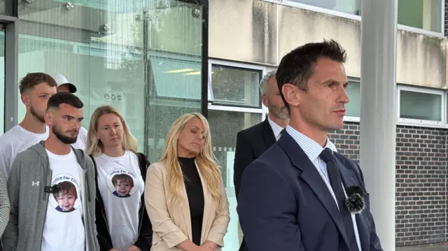 Det Supt Chris Bell from North Wales Police stands on the steps giving a statement while Ethan's family stand behind him.