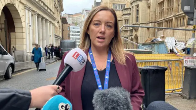 Det Ch Insp Nadine Partridge outside Bristol Crown Court. She has blonde hair and is wearing a burgundy jacket and black top with a blue lanyard. Four camera mics are at the bottom of the frame.