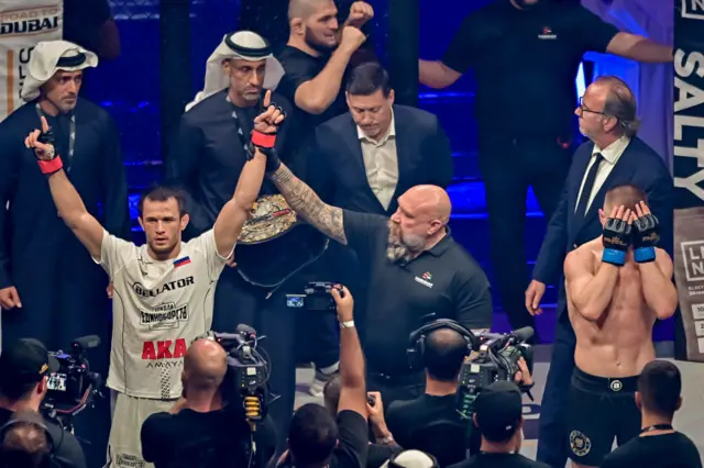 Usman Nurmagomedov with his hands up and Paul Hughes with his hands over his face