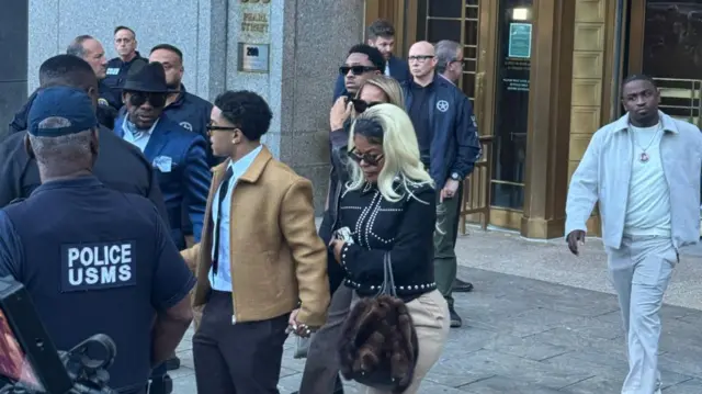 Man in tan jacket and black pants holds hands with woman in black jacket and tan pants