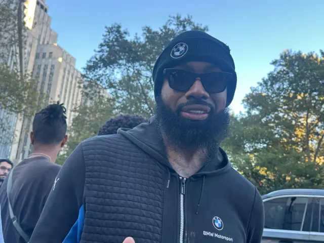 Man with black beanie that has a BMW patch, sunglasses, beard and black BMW hoodie