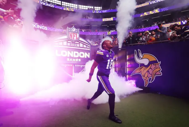 Justin Jefferson runs out of the tunnel at Tottenham Hotspur Stadium, surrounded by Minnesota Vikings branding and purple smoke