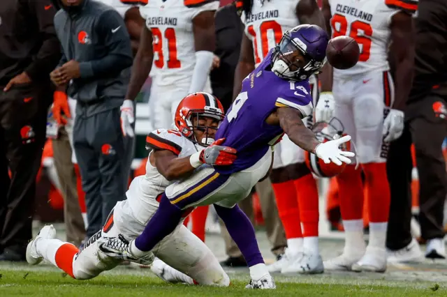 Stefon Diggs dives to catch the ball for Minnesota Vikings, with a Cleveland Browns player tackling him, in front of other Browns players on the sideline