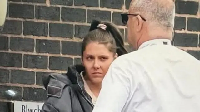 Shannon Ives outside a brick building at an appearance in court in June. A man in a white shirt stands in front of her.