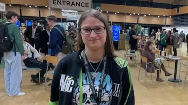 Cate James-Hodges in a black t shirt and black and green hoodie.