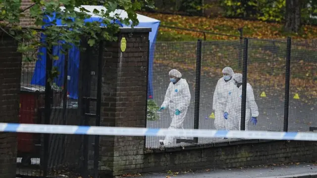 Three forensic officers wearing white overalls and masks remain at the scene near Heaton Park Hebrew Congregation synagogue. A tent has been erected and a police cordon is in place"