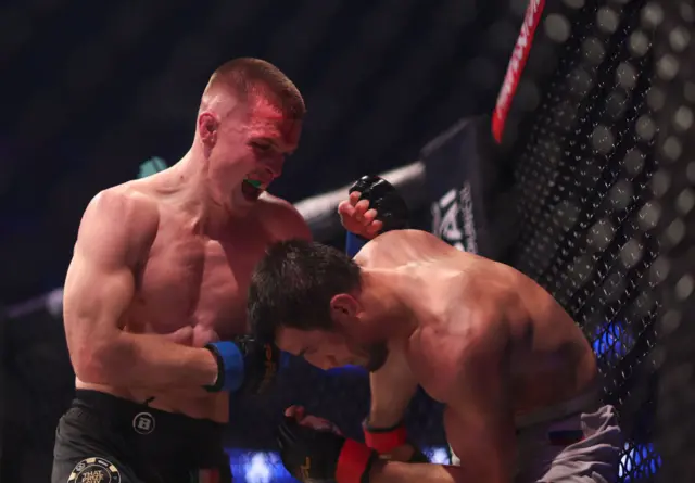 Paul Hughes punching Usman Nurmagomedov up against the cage