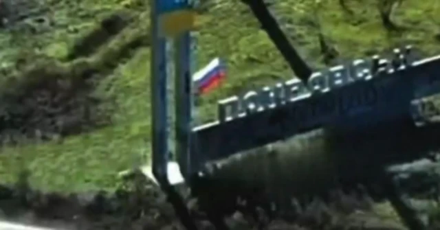 Sign which says Pokrovsk in Ukrainian with cyrillic lettering. A russian flag has been placed near to the Ukrainian flag that forms part of the monument.