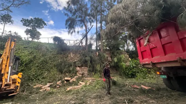 A man stands amid downed tress and debris alongside two large utility vehicles in the aftermath of Hurricane Melissa