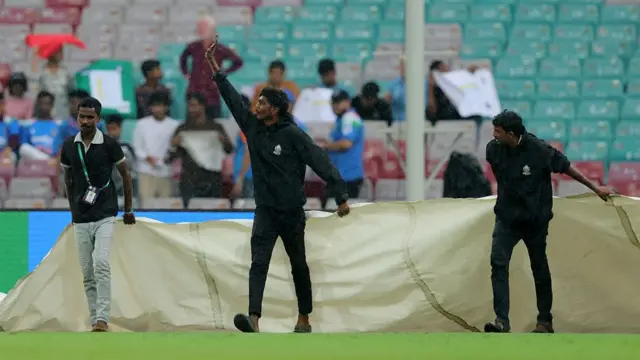 Ground staff bring on the covers as rain interrupts play during the ICC Women's Cricket World Cup India 2025 Semi-Final match between India and Australia