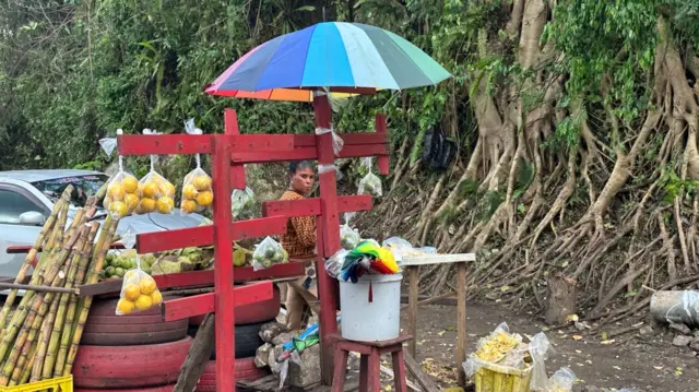 A bright red mango stand with a rainbow coloured umbrella by the side of a road in Jamaica