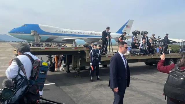 Air Force One plane in the background as cameras line up in front of it