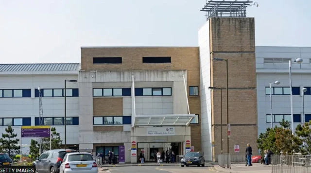 The maternity unit at the Royal Infirmary of Edinburgh, a modern hospital building with a central entrance and tall tower, where more than 5,000 births take place each year. Several people and cars are visible outside.
