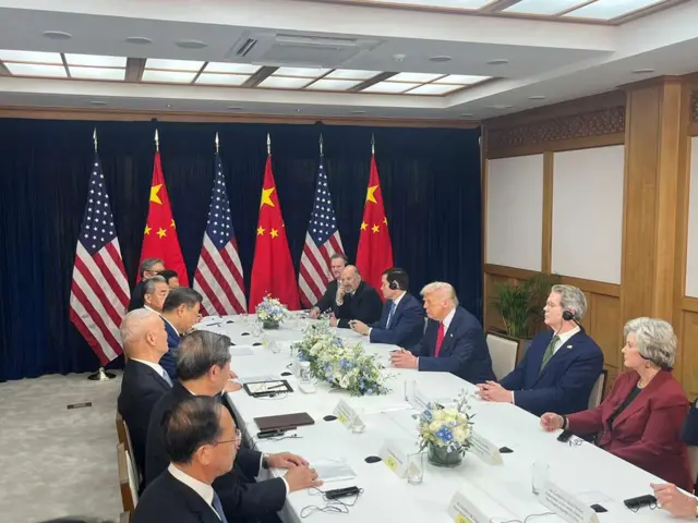 Xi Jinping and Donald Trump, flanked by their officials, meeting face to face while all seated on a long white table