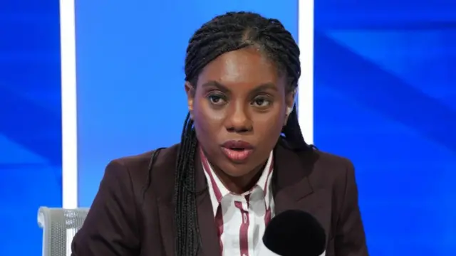 Kemi Badenoch sits at a micrphone