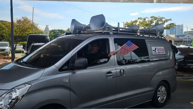 A man in a grey van waving a US flag through the window