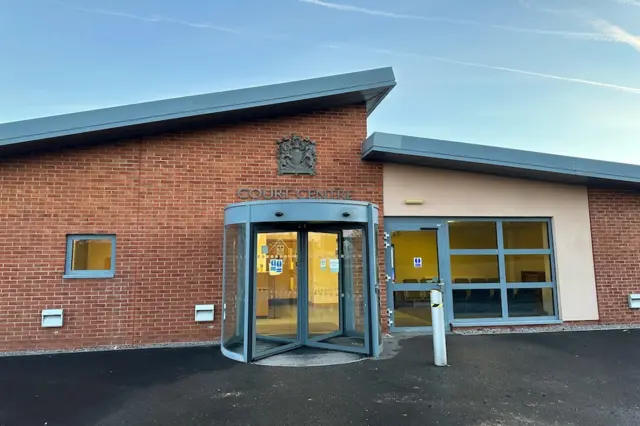 The exterior entrance to the military court in Bulford, Wiltshire. It is a brown brick building with a revolving glass door and an angular ceiling.