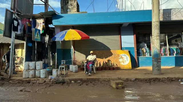 a man sits in a chair beside a mud-filled road