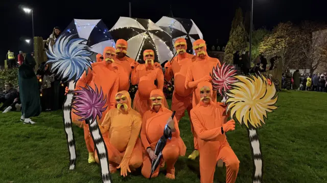 A group of people are dressed in bright orange one piece suits