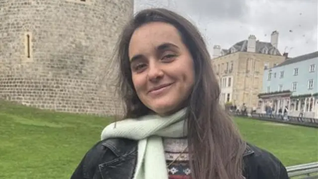 A woman in a black jacket and light green scarf with long brown hair