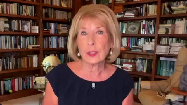 Jennie Bond in black dress answers questions while sitting in a private library