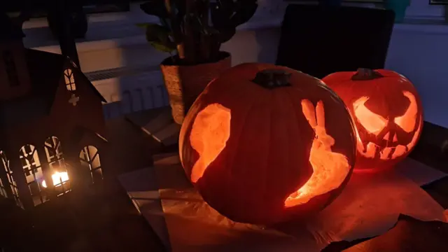 Two carved pumpkins sit on a table at night.
