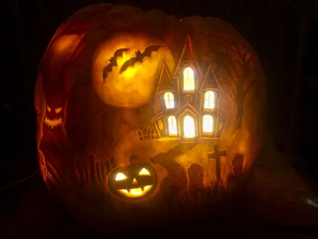A detailed carving into the side of an enormous pumpkin.