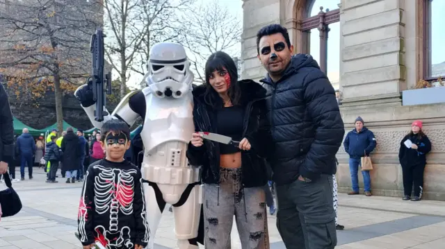 Three people stand with a character from Starwars