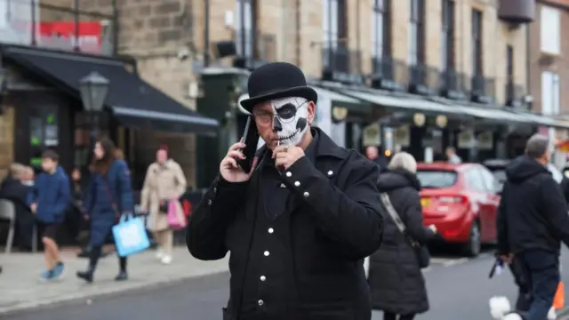 A man in face paint sucks a sweet on a street in Whitby, England.
