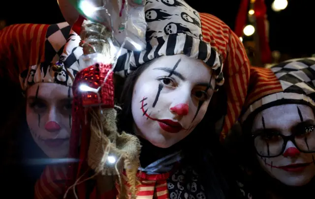 Three young girls are dressed as clowns with detailed facepaint and elaborate hats