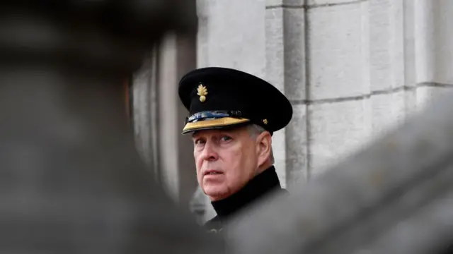 Prince Andrew wearing a hat looks towards the camera. Only his head and neck are visible.